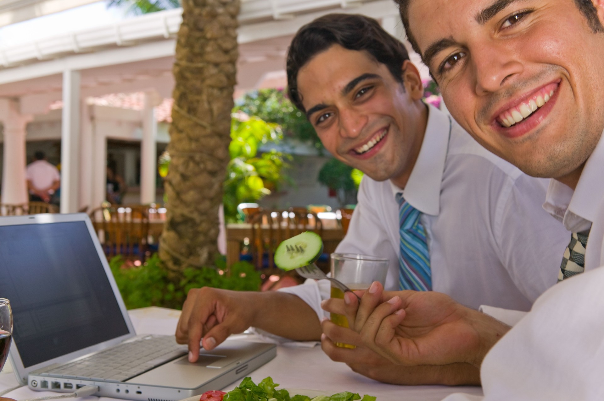 Two businessmen sitting in outdoor cafe with laptop computer